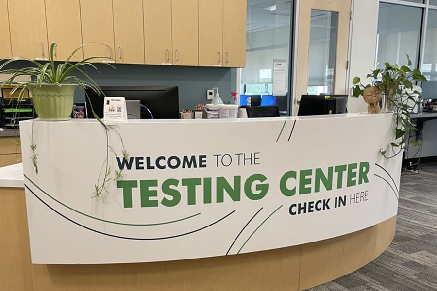 A clean, modern white check-in desk featuring green text that reads Welcome to the Testing Center, Check In Here.